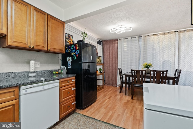 kitchen with dishwasher, black refrigerator, light hardwood / wood-style floors, a textured ceiling, and dark stone counters