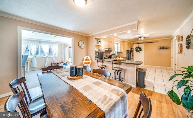 dining room featuring ornamental molding, light hardwood / wood-style flooring, and a textured ceiling