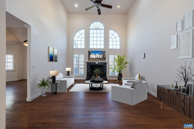 living room featuring a wealth of natural light, dark wood-type flooring, a premium fireplace, and a high ceiling