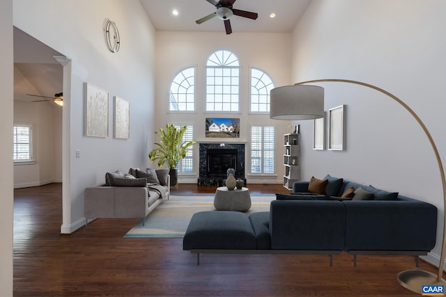 living room featuring dark wood-type flooring, a towering ceiling, a premium fireplace, and ceiling fan