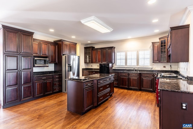 kitchen with crown molding, light wood-type flooring, dark stone counters, a kitchen island, and stainless steel appliances