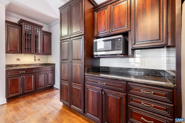 kitchen featuring ornamental molding, dark stone counters, decorative backsplash, and light wood-type flooring