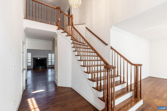 staircase with wood-type flooring, a towering ceiling, and crown molding