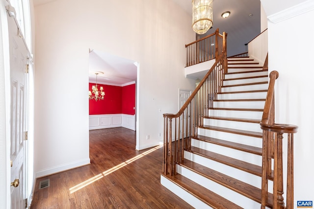 staircase with hardwood / wood-style flooring, crown molding, a high ceiling, and a chandelier