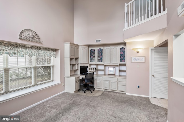 office space with a high ceiling, built in desk, and light colored carpet