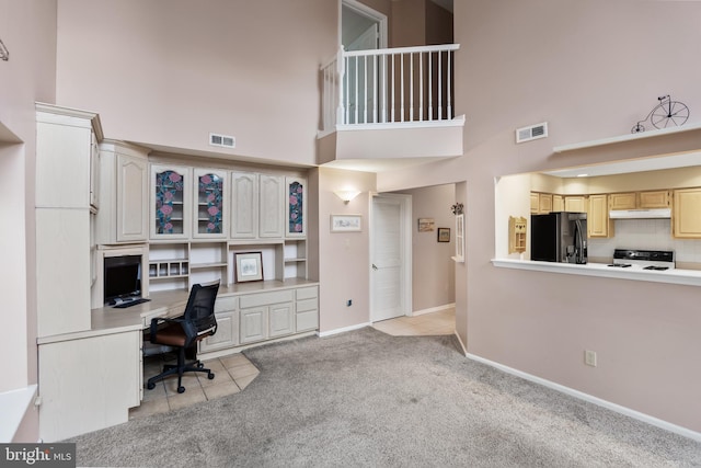 office area with light carpet, a towering ceiling, and built in desk