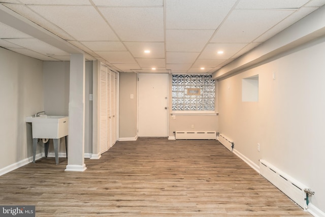 basement featuring a baseboard radiator, a paneled ceiling, and light wood-type flooring