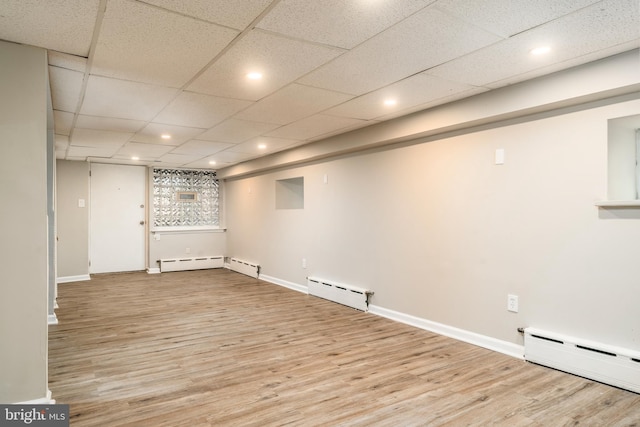 basement featuring a drop ceiling, a baseboard radiator, and light hardwood / wood-style floors