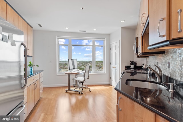 kitchen with sink, light hardwood / wood-style flooring, dark stone countertops, backsplash, and stainless steel appliances