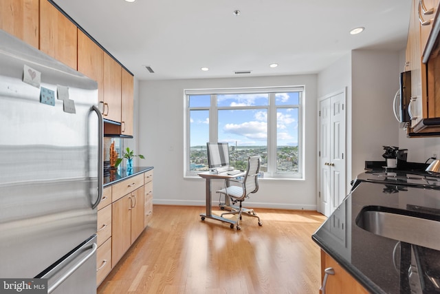 kitchen with appliances with stainless steel finishes, light hardwood / wood-style floors, light brown cabinets, and dark stone counters