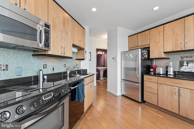 kitchen with sink, appliances with stainless steel finishes, dark stone countertops, tasteful backsplash, and light wood-type flooring