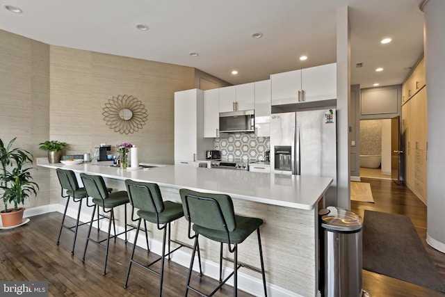 kitchen with dark wood-style floors, light countertops, appliances with stainless steel finishes, and a breakfast bar