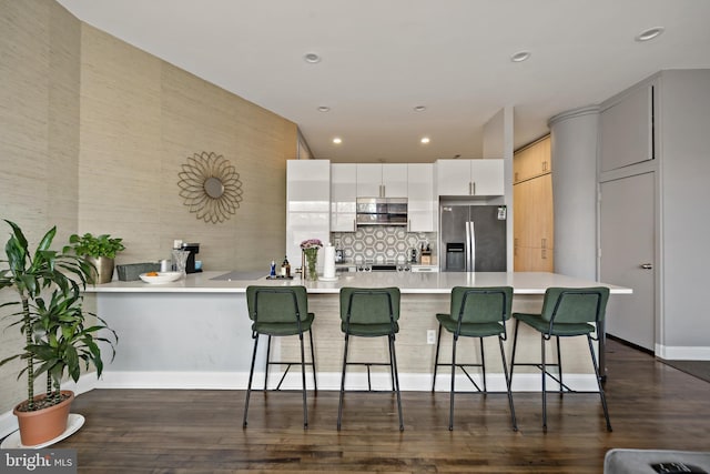 kitchen with dark wood finished floors, a breakfast bar area, light countertops, stainless steel fridge, and a peninsula