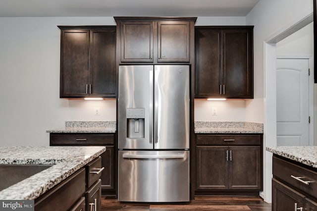 kitchen with dark brown cabinets, stainless steel fridge, light stone countertops, and dark hardwood / wood-style floors