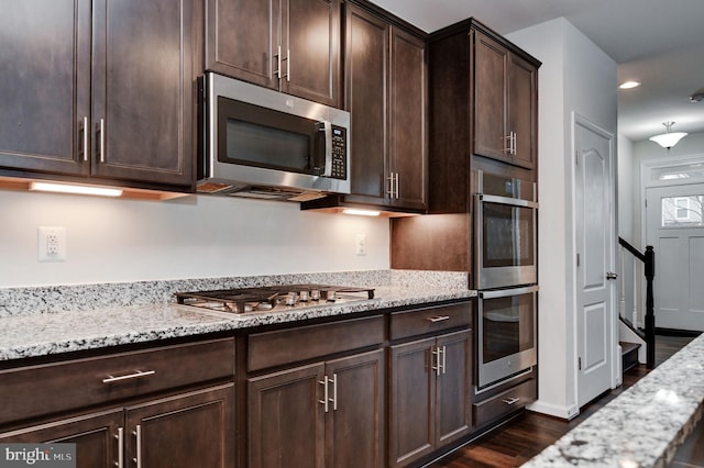 kitchen with dark hardwood / wood-style floors, appliances with stainless steel finishes, dark brown cabinets, and light stone counters