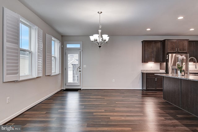 kitchen featuring light stone counters, an inviting chandelier, decorative light fixtures, dark brown cabinets, and dark hardwood / wood-style floors