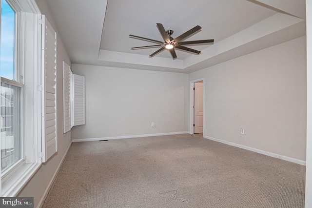 carpeted spare room with a raised ceiling and ceiling fan