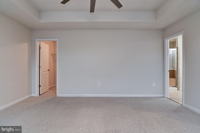 carpeted spare room with a raised ceiling and ceiling fan