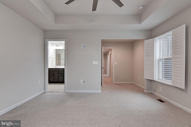 unfurnished bedroom featuring a tray ceiling, ensuite bath, and light colored carpet