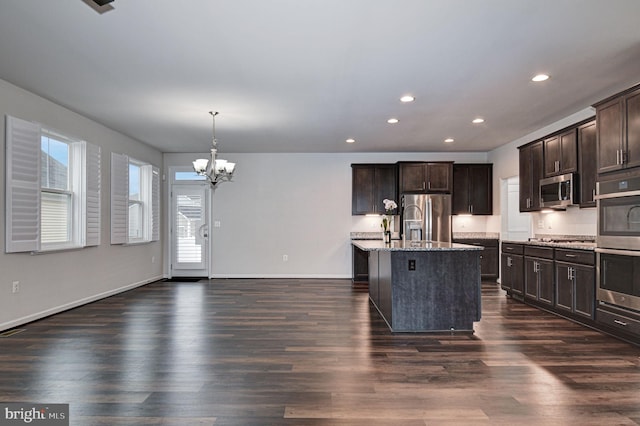 kitchen with appliances with stainless steel finishes, a kitchen island with sink, dark brown cabinetry, and decorative light fixtures