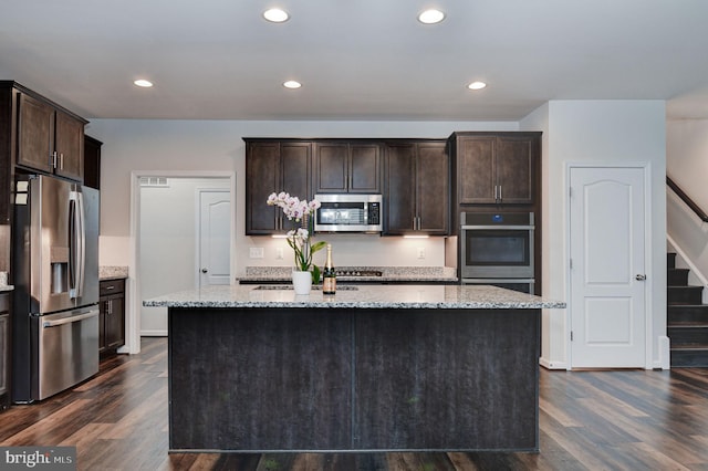 kitchen with dark brown cabinetry, light stone countertops, an island with sink, and appliances with stainless steel finishes