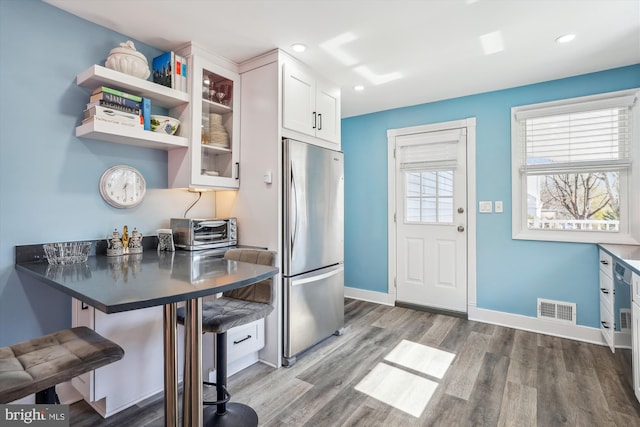 kitchen featuring visible vents, glass insert cabinets, freestanding refrigerator, white cabinets, and wood finished floors