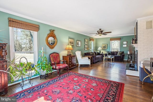 living area with a ceiling fan, a fireplace, ornamental molding, and wood finished floors