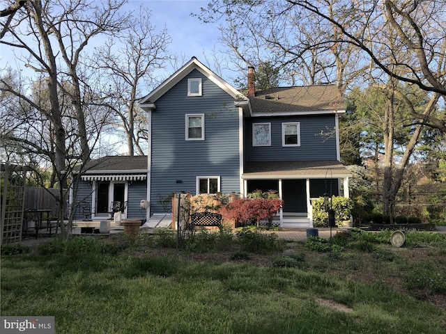 rear view of property with a shingled roof, a chimney, and a yard