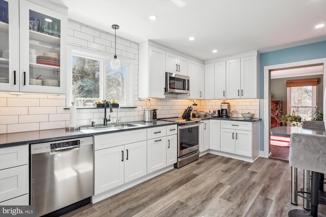 kitchen with stainless steel appliances, wood finished floors, dark countertops, and a sink