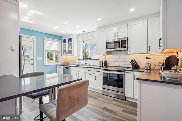 kitchen featuring dark countertops, light wood-type flooring, appliances with stainless steel finishes, and a sink