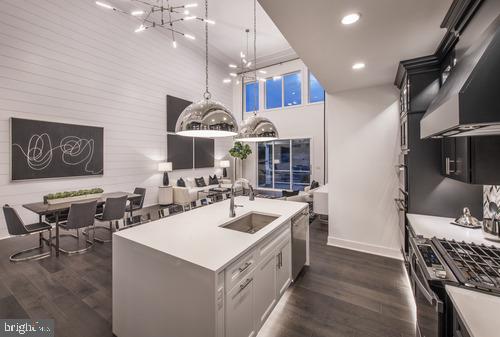 kitchen with dark hardwood / wood-style floors, pendant lighting, sink, stainless steel appliances, and a center island with sink