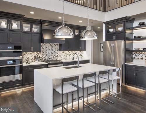 kitchen featuring sink, dark wood-type flooring, appliances with stainless steel finishes, an island with sink, and decorative light fixtures