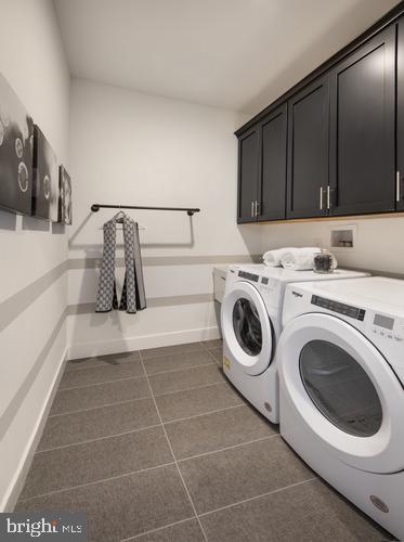 laundry area with dark tile patterned flooring, washer and clothes dryer, and cabinets