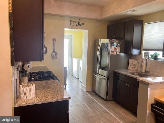 kitchen featuring sink, decorative backsplash, light stone countertops, and stainless steel refrigerator