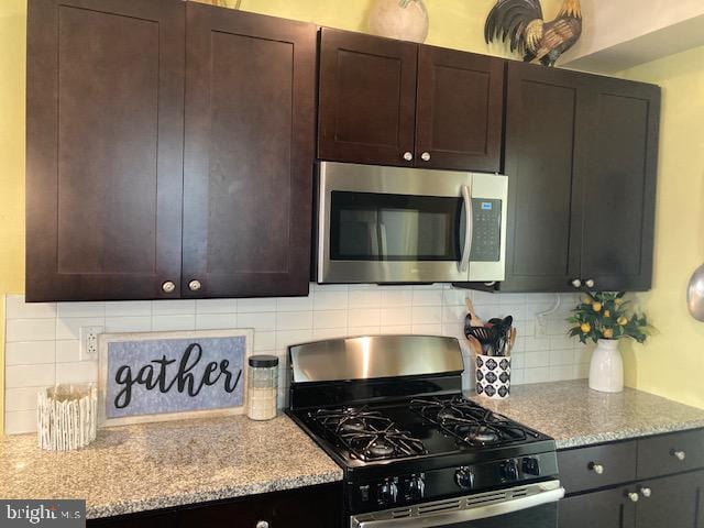 kitchen featuring dark brown cabinetry, backsplash, light stone countertops, and gas range oven