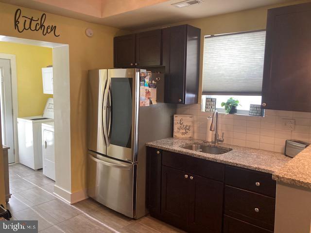 kitchen with sink, dark brown cabinets, stainless steel fridge, independent washer and dryer, and decorative backsplash