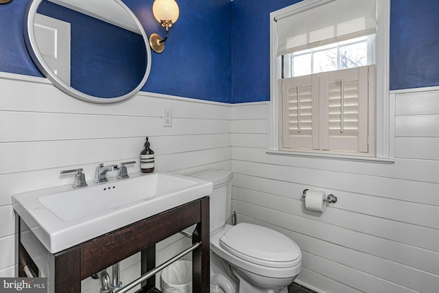 half bathroom with toilet, a wainscoted wall, and a sink