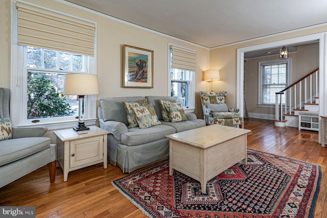 living room featuring baseboards, crown molding, stairway, and light wood finished floors