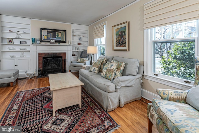 living area with a brick fireplace, baseboards, built in features, and hardwood / wood-style floors