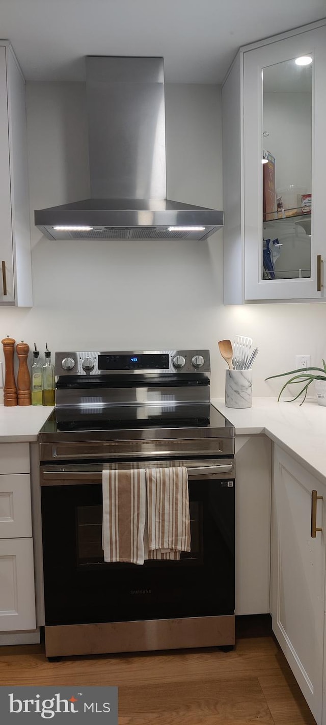 kitchen with white cabinetry, electric stove, light hardwood / wood-style flooring, and wall chimney exhaust hood