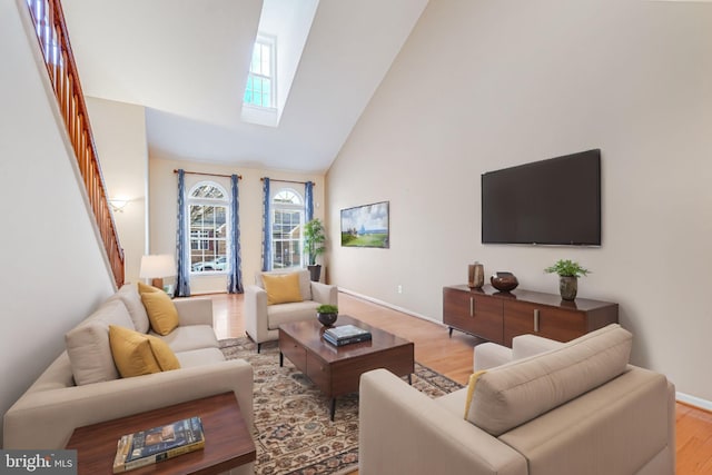 living area with high vaulted ceiling, a skylight, light wood finished floors, baseboards, and stairs