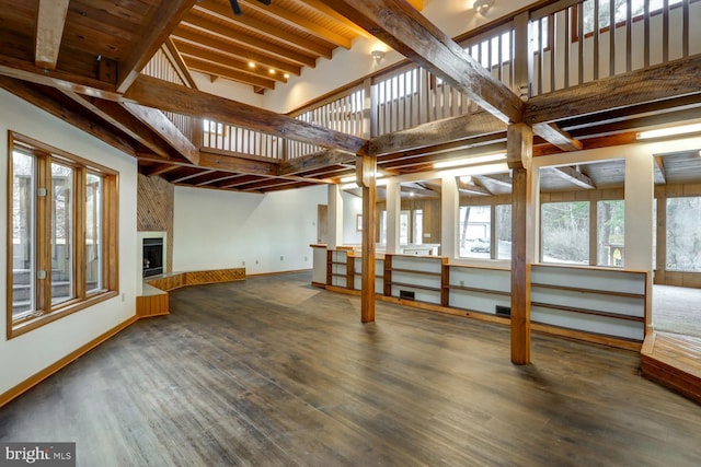 unfurnished living room featuring beam ceiling, a towering ceiling, dark hardwood / wood-style floors, a fireplace, and wooden ceiling