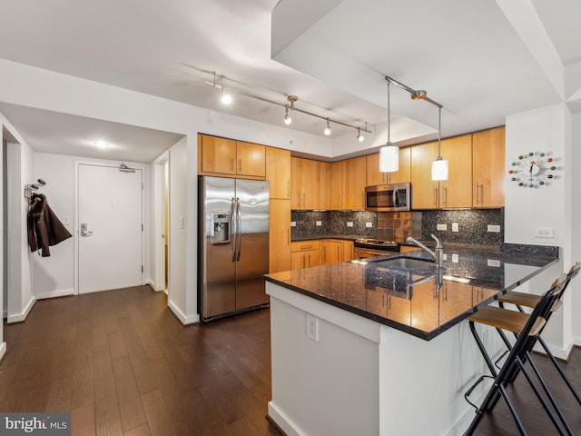 kitchen featuring stainless steel appliances, hanging light fixtures, dark stone countertops, and kitchen peninsula