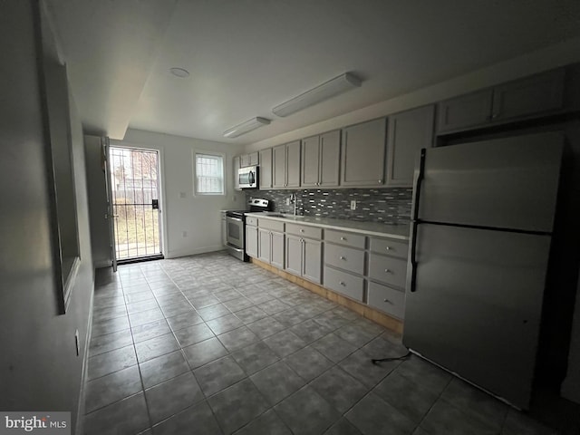 kitchen with sink, tasteful backsplash, light tile patterned floors, gray cabinets, and stainless steel appliances