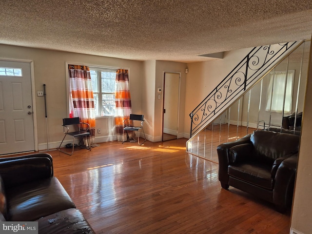 living area featuring baseboards, a textured ceiling, stairway, and wood finished floors