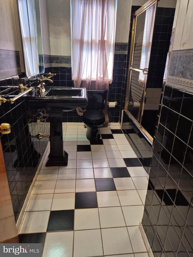 bathroom with toilet, a wainscoted wall, tile patterned floors, a shower stall, and tile walls