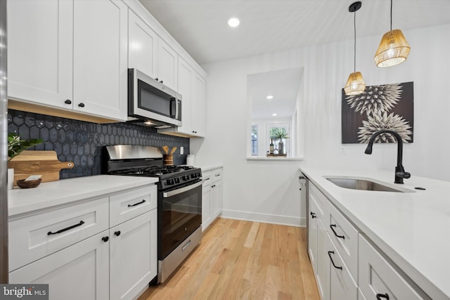 kitchen featuring sink, white cabinetry, decorative light fixtures, light wood-type flooring, and stainless steel appliances