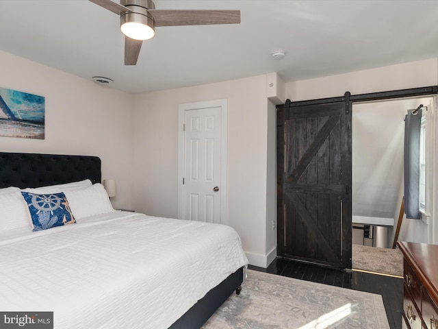 bedroom with a barn door, dark wood-type flooring, and ceiling fan