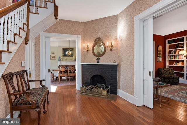 sitting room with hardwood / wood-style flooring, a brick fireplace, and an inviting chandelier