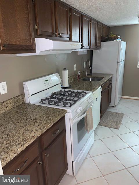 kitchen featuring light tile patterned flooring, sink, white appliances, dark brown cabinetry, and a textured ceiling